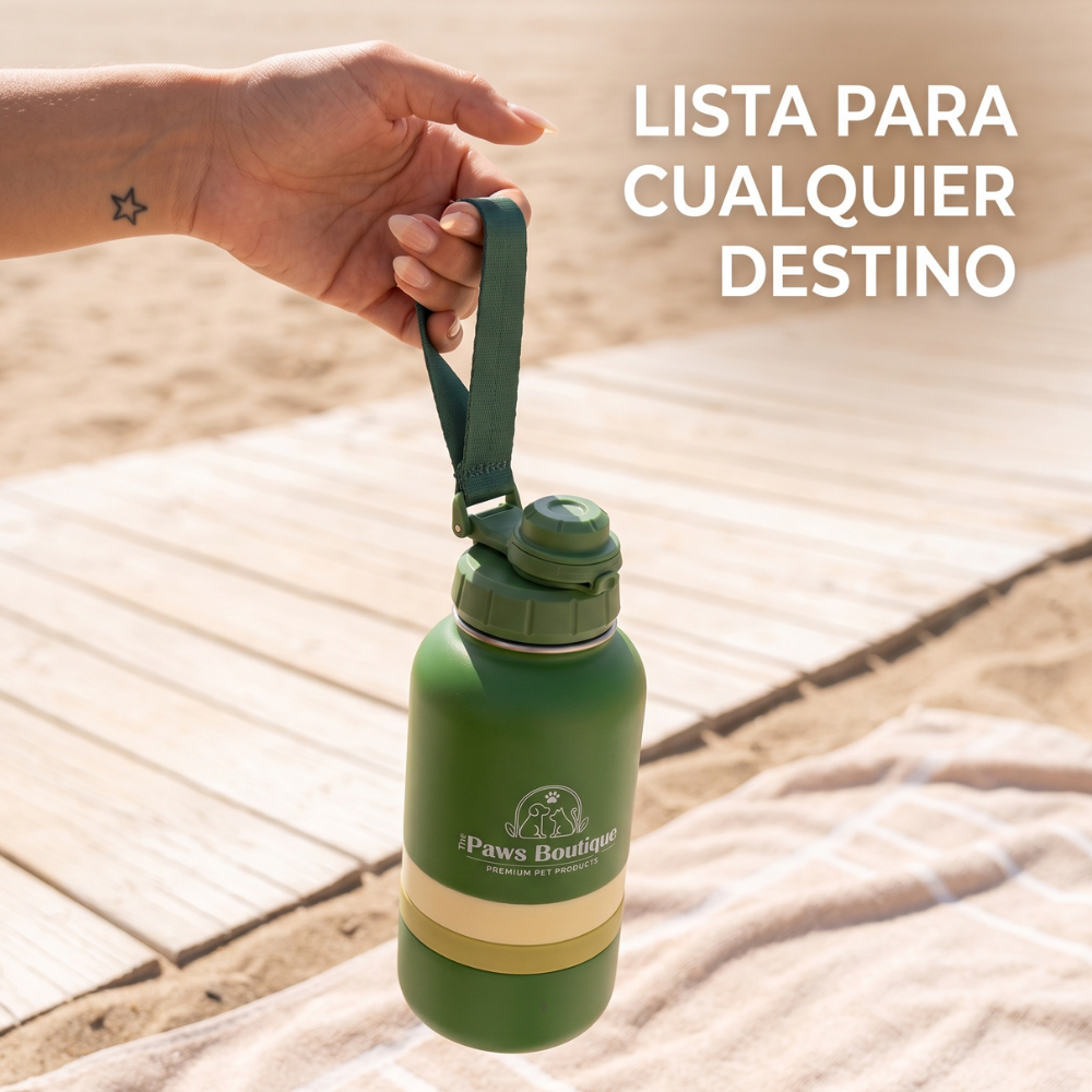 Mano sosteniendo por el asa la botella bebedero portátil para perros en la playa. El accesorio de viaje premium definitivo de The Paws Boutique